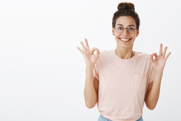 Aufgeregtes schönes Mädchen mit Brille, die gegen die weiße Wand aufwirft