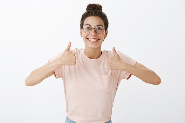 Aufgeregtes schönes Mädchen mit Brille, die gegen die weiße Wand aufwirft