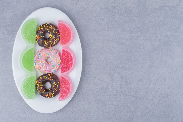 Aufgereihte Donuts und Marmeladen auf einer Platte auf Marmoroberfläche
