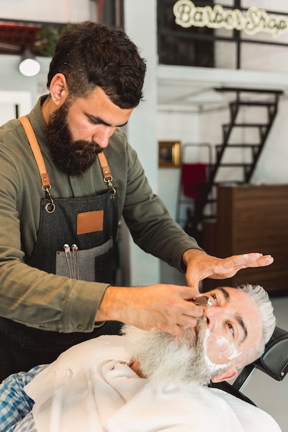 Aufmerksamer Friseur, der dem Kunden im Friseursalon Bart rasiert