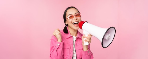 Aufmerksamkeitsankündigungskonzept Begeistertes asiatisches Mädchen, das in Megaphonwerbung schreit, wobei Lautsprecher rekrutiert werden, die über rosafarbenem Hintergrund stehen