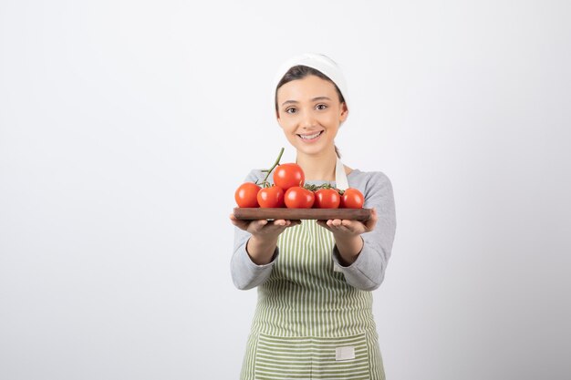 Aufnahme einer entzückenden jungen Frau, die einen Teller mit roten Tomaten über einer weißen Wand hält?
