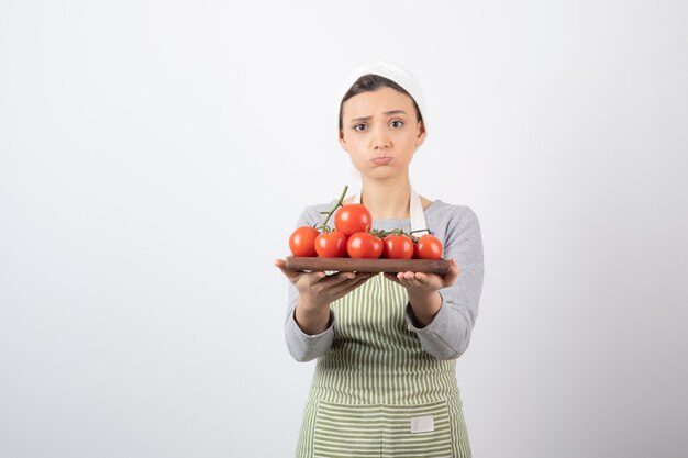 Aufnahme einer entzückenden jungen Frau, die Teller mit roten Tomaten über weißer Wand anbietet?
