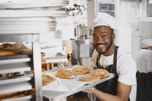 Aufnahme eines gutaussehenden Bäckers, der in der Backfertigung Tabletts mit frischem Brot auf den Stand stellt. Afroamerikaner.