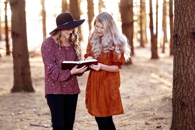 Aufnahme von zwei jungen Frauen, die mit einem Buch im Wald posieren, Herbststimmung