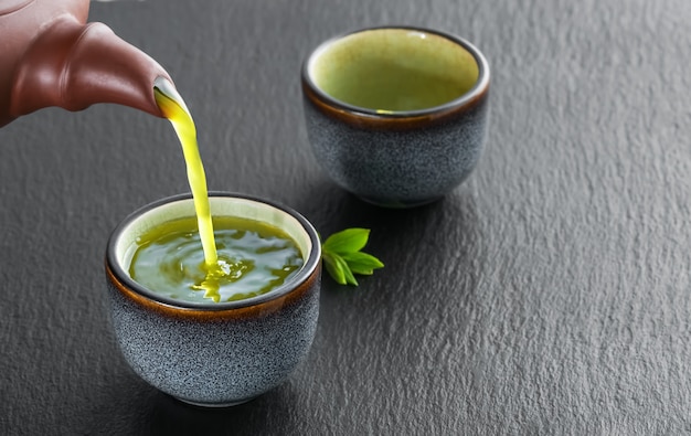 Aus der teekanne wird heißer grüner tee in die blaue schüssel gegossen