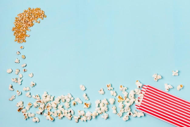 Aus Maissamen werden Popcorns, die vor blauem Hintergrund in die Popcornbox gelangen