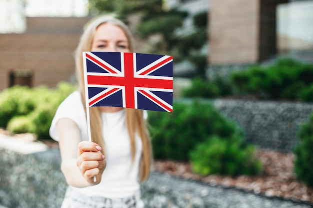 Ausbildung im ausland. studentenmädchen bedeckt ihr gesicht mit einer kleinen britischen britischen flagge und steht in der nähe der universität auf der straße. py space