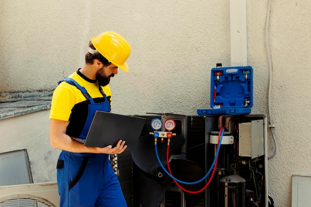 Kostenloses Foto ausgebildeter ingenieur mit der aufgabe, die internen komponenten von klimaanlagen im freien zu warten, den freon-niveau zu überprüfen und thermostate zu kalibrieren, erfahrener techniker, der den wartungsplan auf einem laptop überprüft