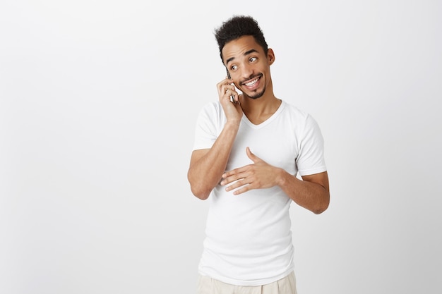 Ausgehender hübscher schwarzer Mann im weißen T-Shirt, der am Telefon spricht, lächelnd, glückliches Gespräch