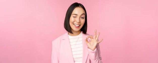 Ausgezeichnete Arbeit gut gemachte Geste Lächelnde asiatische Geschäftsfrau, die ein okay-ok-Zeichen zeigt, lobt gute Arbeit, die ein Unternehmen empfiehlt, das als selbstbewusster professioneller rosafarbener Hintergrund aussieht