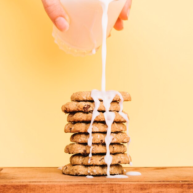 Auslaufende Milch der Person vom Glas auf Plätzchenstapel