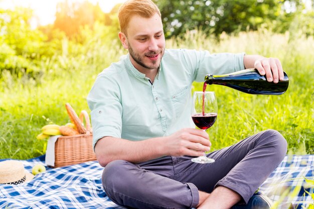 Auslaufender Wein des Mannes, der auf Picknickdecke sitzt