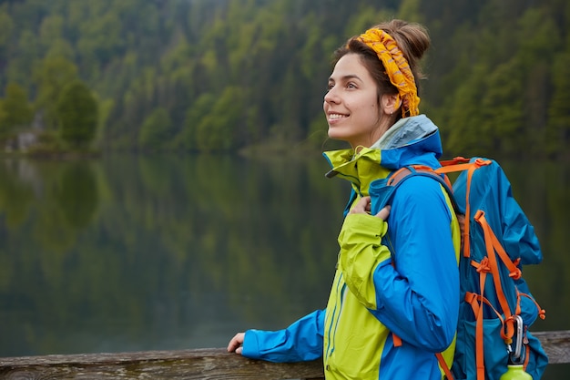 Außenansicht der glücklichen aktiven weiblichen Wanderungen nahe See und grünem Wald