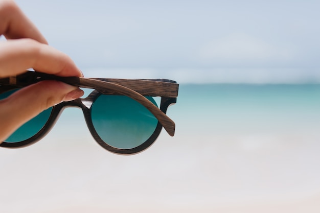 Außenfoto des Ozeans mit weiblicher Hand auf Vordergrund. Frau, die Sommersonnenbrille auf See hält.