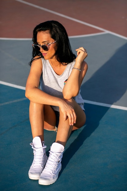 Außenporträt der brünetten Frau, die am Sportspielplatz posiert, lässiges Outfit.