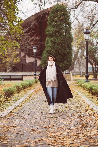 Außenporträt der Frau im Park, der schwarzen Wintermantel und weißen Schal trägt