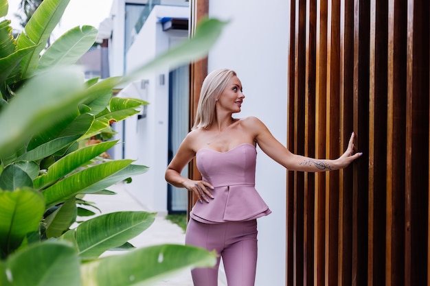 Außenporträt der stilvollen europäischen Frau auf rosa Modeanzug außerhalb der Villa