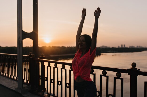 Außenporträt des gewinnenden Mädchens im rosa T-Shirt, das am Abend streckt. Blithesome kaukasische Frau, die Yoga tut