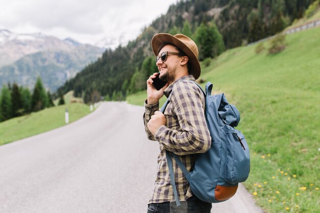 Außenporträt des Mannes mit Smartphone in der Hand, die die Straße mit blauem Rucksack entlang geht