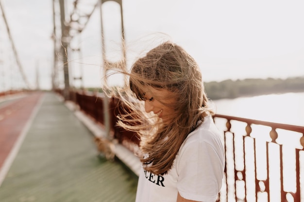 Kostenloses Foto außenporträt eines ansprechenden mädchens, das mit wunderbaren glücklichen emotionen lächelt und das gesicht mit fliegenden haaren bedeckt