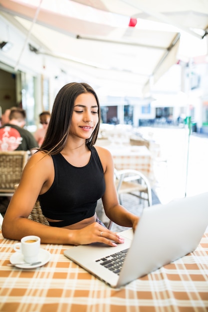 Außerhalb arbeiten. Schöne junge Frau im funky Hut, der am Laptop arbeitet und lächelt, während draußen sitzt