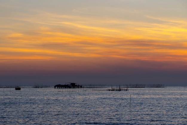 Austernbauernhof im Sonnenunterganghintergrund des Meeres und des schönen Himmels