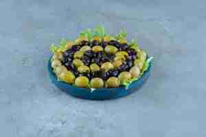 Kostenloses Foto auswahl an oliven auf einer mit salat bedeckten platte auf marmoroberfläche