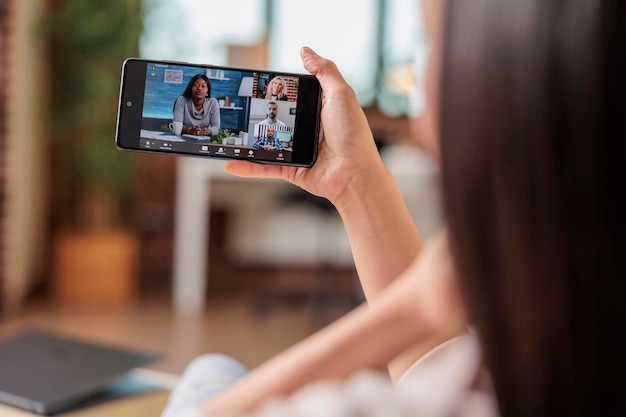 Authentische beschäftigte asiatische Frau auf Videoanruf, die Online-Kommunikationsarbeit von zu Hause aus spricht und mit der mobilen App winkt