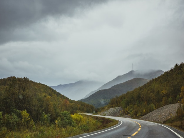 Autobahn in der Nähe des Waldes in den Bergen unter dem dunklen bewölkten Himmel