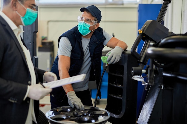 Automanager und Wartungsingenieur tragen Gesichtsmasken, während sie während der Coronavirus-Epidemie in der Autowerkstatt arbeiten