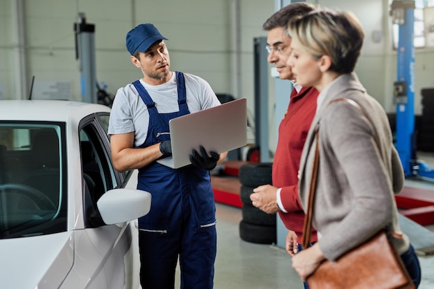 Automechaniker, der mit seinen Kunden kommuniziert, während er einen Laptop in einer Werkstatt verwendet