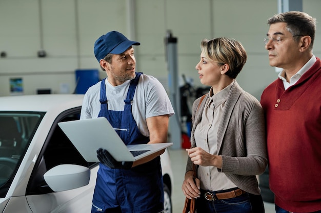 Automechaniker, der mit seinen Kunden kommuniziert, während er einen Laptop in einer Werkstatt verwendet