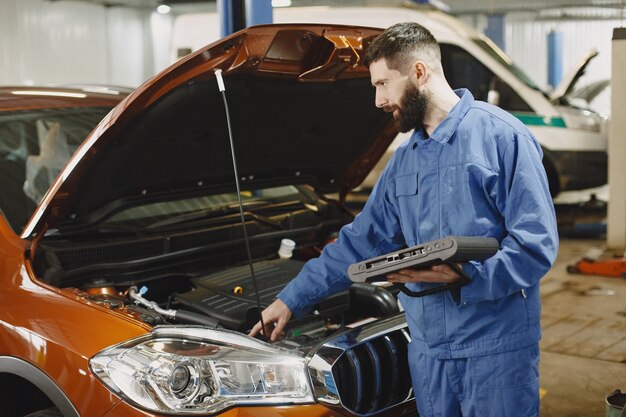 Automechaniker mit einer Tablette nahe Auto in Arbeitskleidung