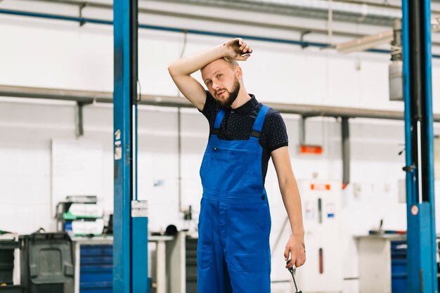 Automechaniker nahe locklift wischendem Schweiß der Front und des Haltens des Schlüssels