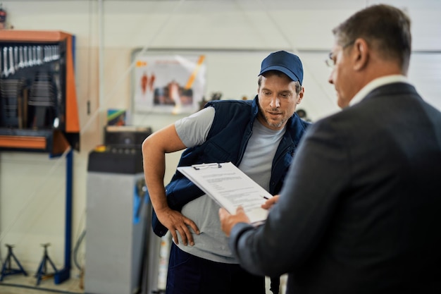 Automechaniker und Geschäftsmann analysieren Berichte während der Arbeit in der Autowerkstatt