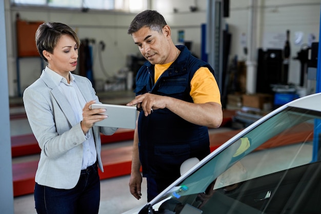 Automechaniker und Managerin kooperieren bei der Arbeit am Touchpad in der Autowerkstatt