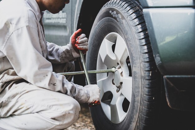 Autoreparaturmann, der eine weiße Uniform steht und einen Schlüssel hält, der ein wesentliches Werkzeug für einen Mechaniker ist