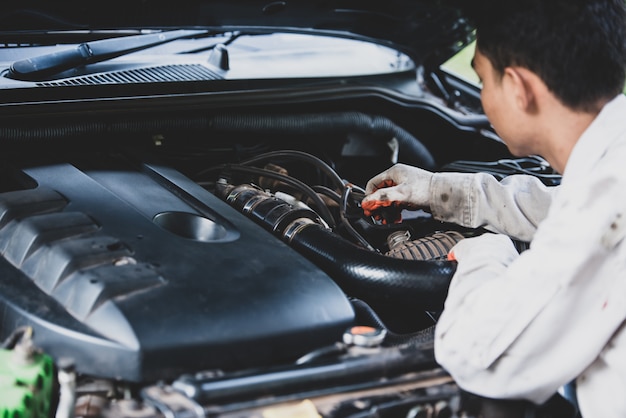 Autoreparaturmann, der eine weiße Uniform steht und einen Schlüssel hält, der ein wesentliches Werkzeug für einen Mechaniker ist