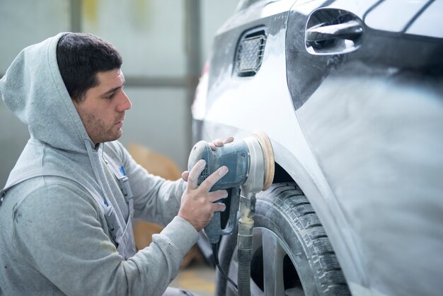 Autoreparaturmann, der Karosserie mit einer Maschine schleift, die Fahrzeug zum Lackieren vorbereitet