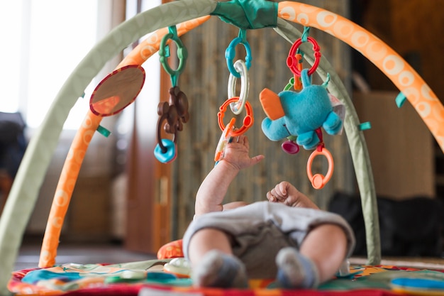Baby, das auf sich entwickelnder Wolldecke mit beweglichen pädagogischen Spielwaren liegt