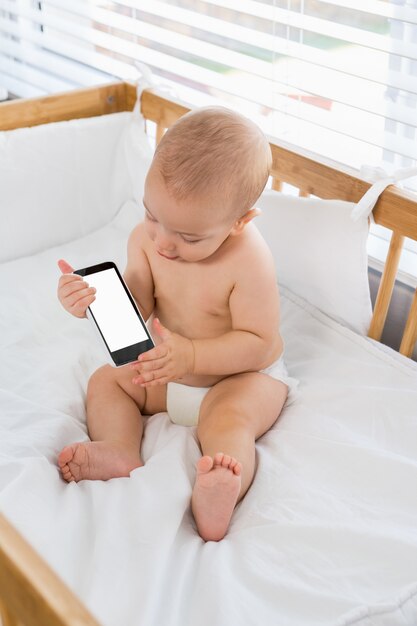 Baby, das mit Mobiltelefon auf einem Wiege spielen