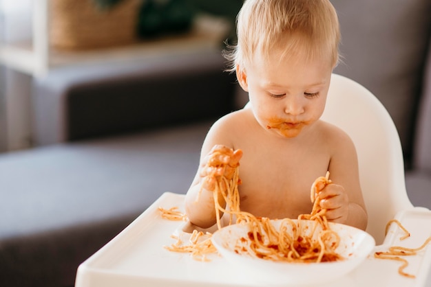 Baby, das nudeln in seinem hochstuhl isst und ein durcheinander macht