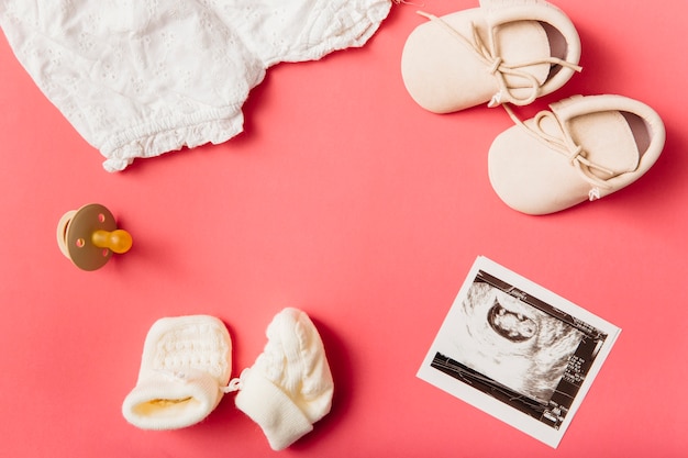 Baby Kleidung; Socken; Schnuller; Paar Schuhe und Ultraschallbild auf Pfirsichhintergrund