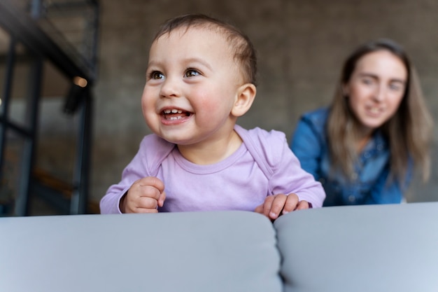 Baby lächelt, während seine defokussierte Mutter ihn beobachtet