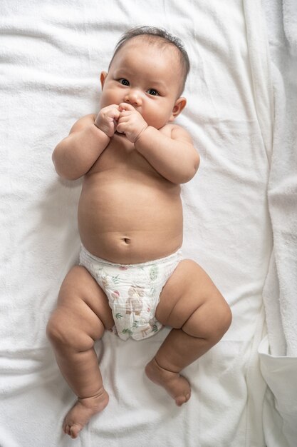 Baby liegend mit dem Gesicht nach oben auf einem weißen Bett