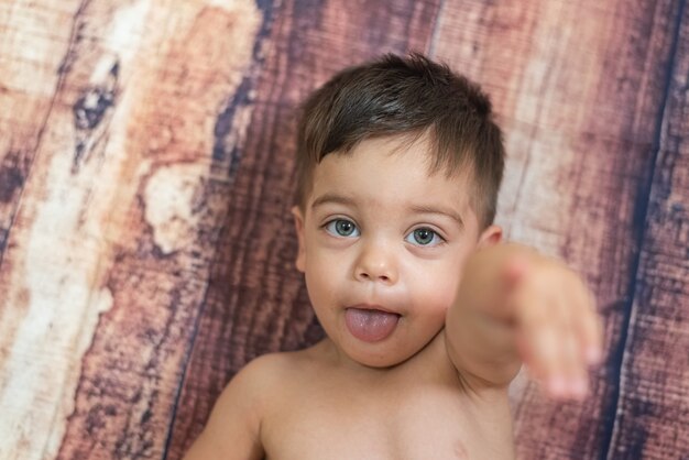 Baby mit blauen Augen, die auf Holzwand mit heraushängender Zunge liegen