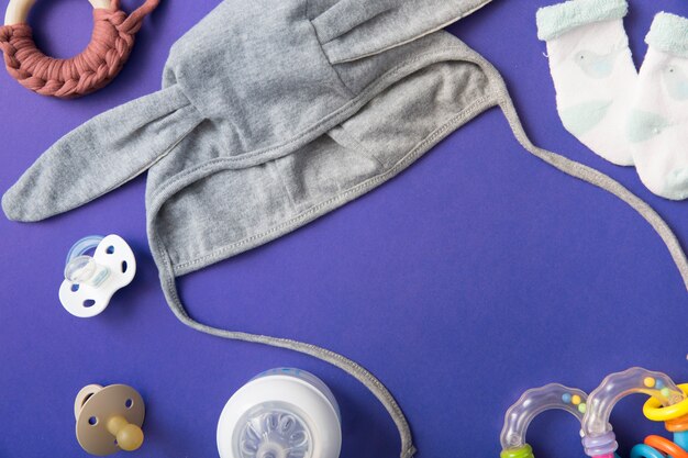 Baby Mütze mit Schnuller; Milchflasche; Spielzeug und Paar Socken auf blauem Hintergrund