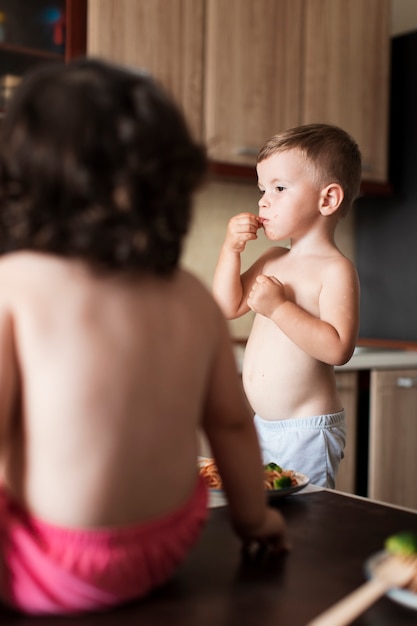 Baby und Junge, die in der Küche sitzen und Teigwaren essen