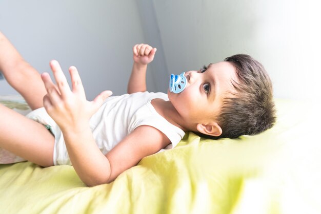 Babyjunge im weißen T-Shirt, das auf Bett liegt